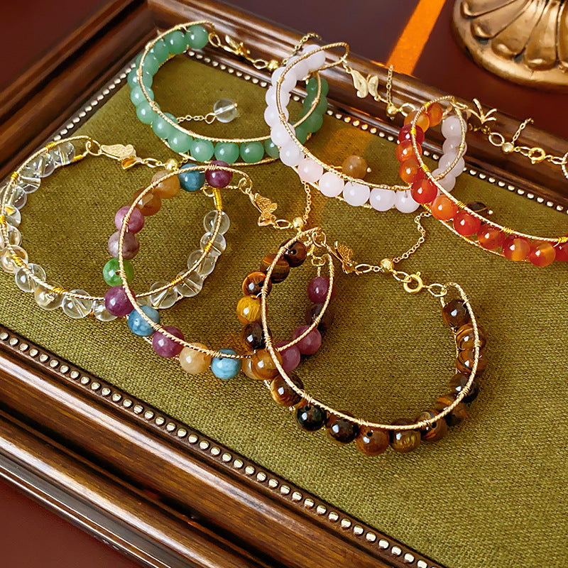 Natural stone beaded bracelets in multiple colors including red agate, rose quartz, and white crystal, with golden accents displayed in a jewelry tray.