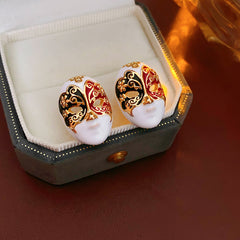 Enamel masquerade face stud earrings with red and black halves and gold filigree on a velvet jewelry box — Venetian Masquerade Studs.