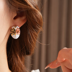 Enamel masquerade face stud earrings with red and black halves and gold filigree on a velvet jewelry box — Venetian Masquerade Studs.