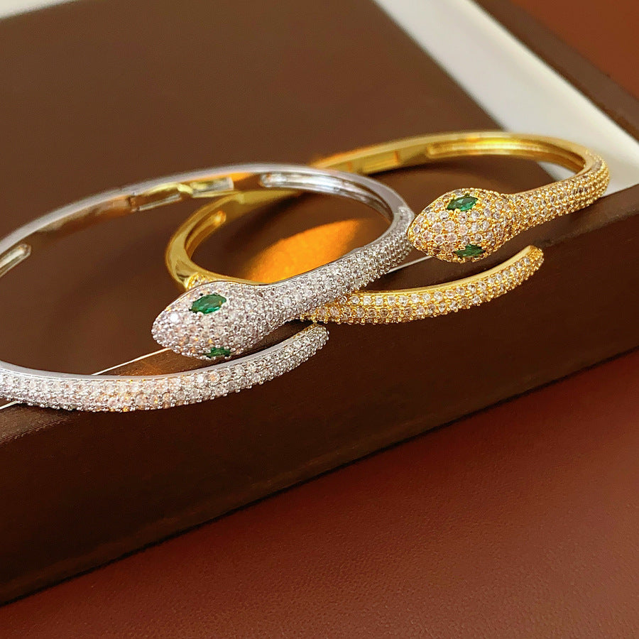 Gold and silver snake-shaped zircon bangles with emerald eyes — Serpent Luxe Bangle by Glazenya.