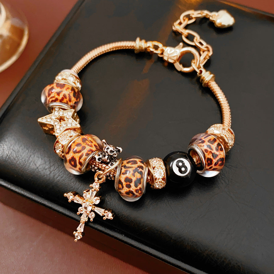 Leopard Cross Luxe Bracelet with leopard-patterned beads, zircon accents, black 8-ball bead, and cross pendant on gold chain