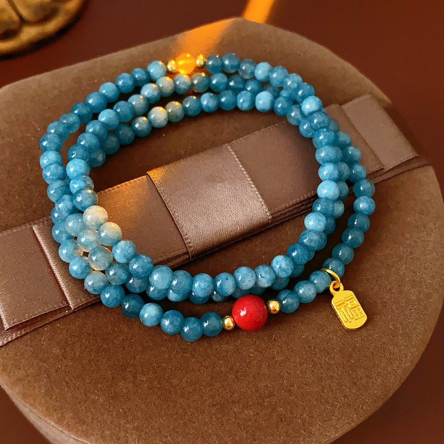 Blue multi-wrap beaded bracelet with red accent bead and gold charm — Azure Charm Wrap Bracelet.