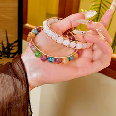 Natural stone beaded bracelets in multiple colors including red agate, rose quartz, and white crystal, with golden accents displayed in a jewelry tray.