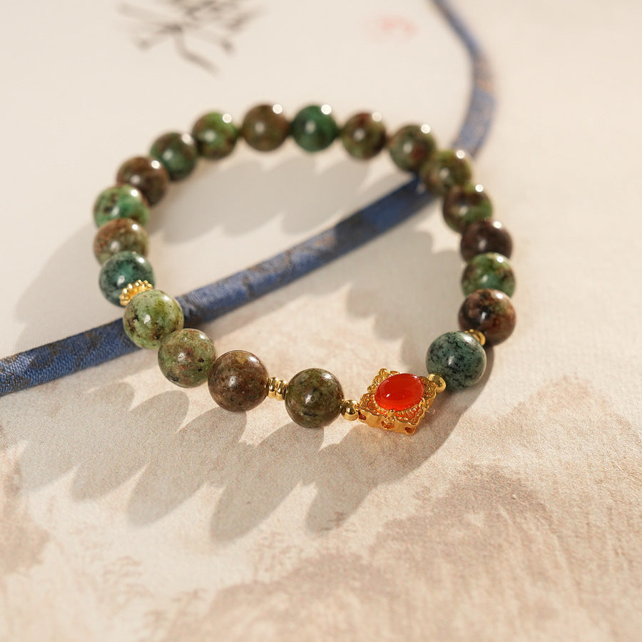 <div class="gz-desc">
  <p>Earthy and refined <strong>natural stone bracelet</strong> combining lush <strong>green ghost</strong> beads with smooth <strong>agate</strong>, accented by a warm red centerpiece and gold-tone spacers for a subtle touch of luxury.</p>

  <h3>Design Story</h3>
  <p>The <strong>Forest Ember Agate Bracelet</strong> evokes the calm of an ancient forest lit by a single ember. Mossy green tones bring grounding energy, while the red accent adds a gentle spark—balance between serenity an