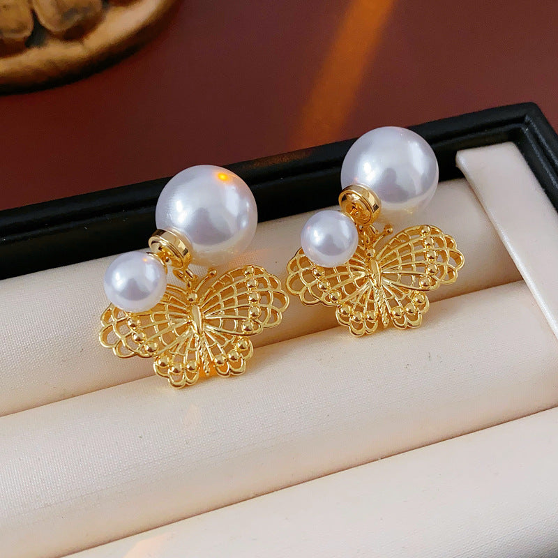 Double-pearl stud earrings with gold-tone butterfly and star charms displayed in a jewelry tray — Double Pearl Charm Studs.
