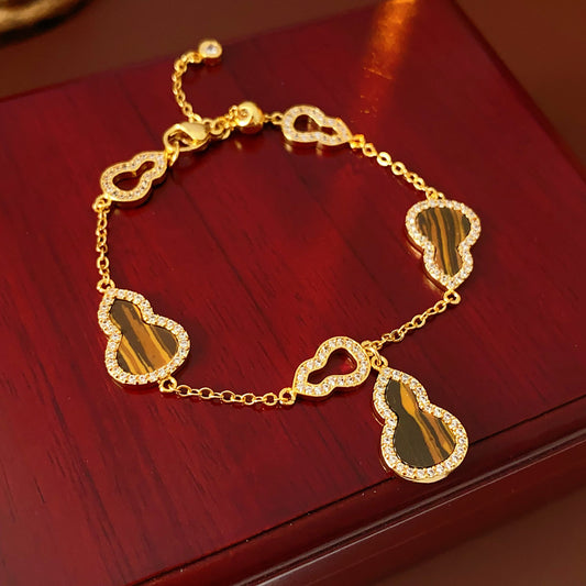 Fortune Gourd Tiger Eye Bracelet with golden gourd motifs, cubic zirconia accents, and natural tiger eye stones, displayed on red wood background