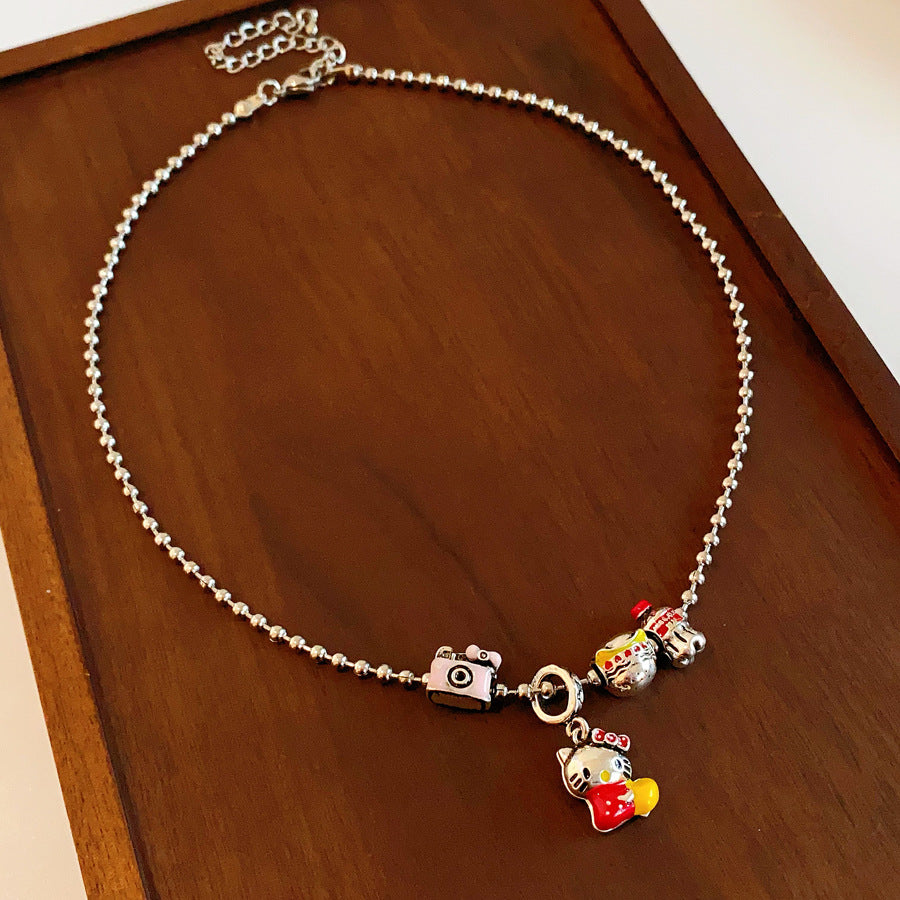 City Voyager Cat Charm Necklace — silver-tone ball chain with enamel cat and camera charms, travel-inspired charm cluster on black pouch