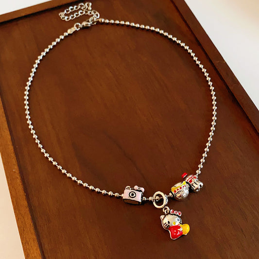 City Voyager Cat Charm Necklace — silver-tone ball chain with enamel cat and camera charms, travel-inspired charm cluster on black pouch