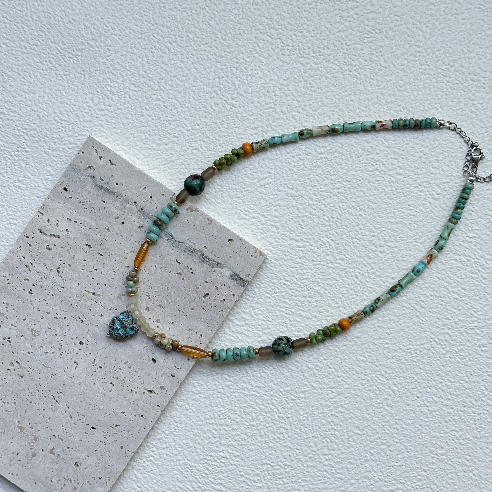 Flat lay of Verdant Owl Necklace on textured card – handcrafted sage–lagoon beads, golden accents, and whimsical owl charm