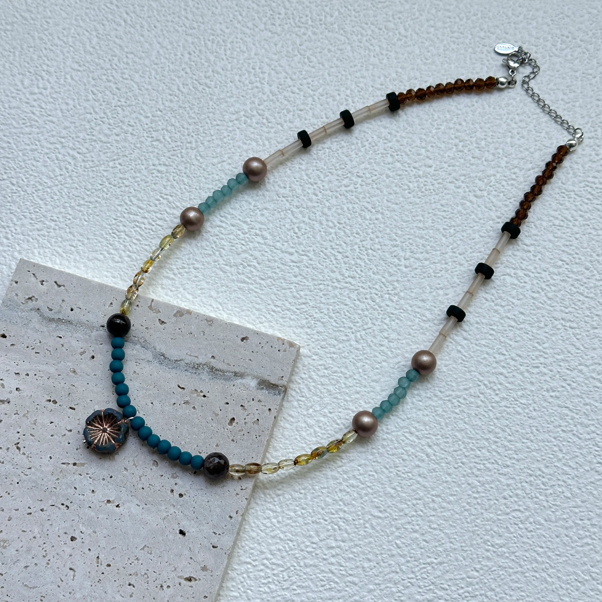 Lagoon Sunburst Necklace displayed on an oval tray – bright lagoon-blue beads and warm golden accents for a sunny seaside look