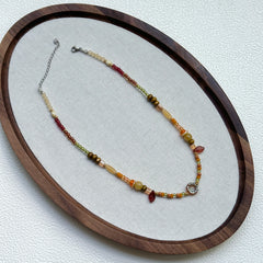 Olive Grove Blossom Necklace displayed on an oval tray – warm olive, amber, and golden beads with floral glass coin centerpiece