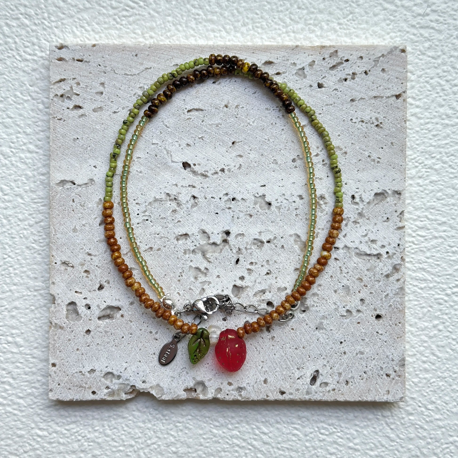Wild Strawberry Necklace styled on a textured card, close-up of strawberry focal with leaf and dewdrop accents – handmade by Glazenya