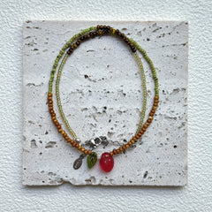 Wild Strawberry Necklace styled on a textured card, close-up of strawberry focal with leaf and dewdrop accents – handmade by Glazenya