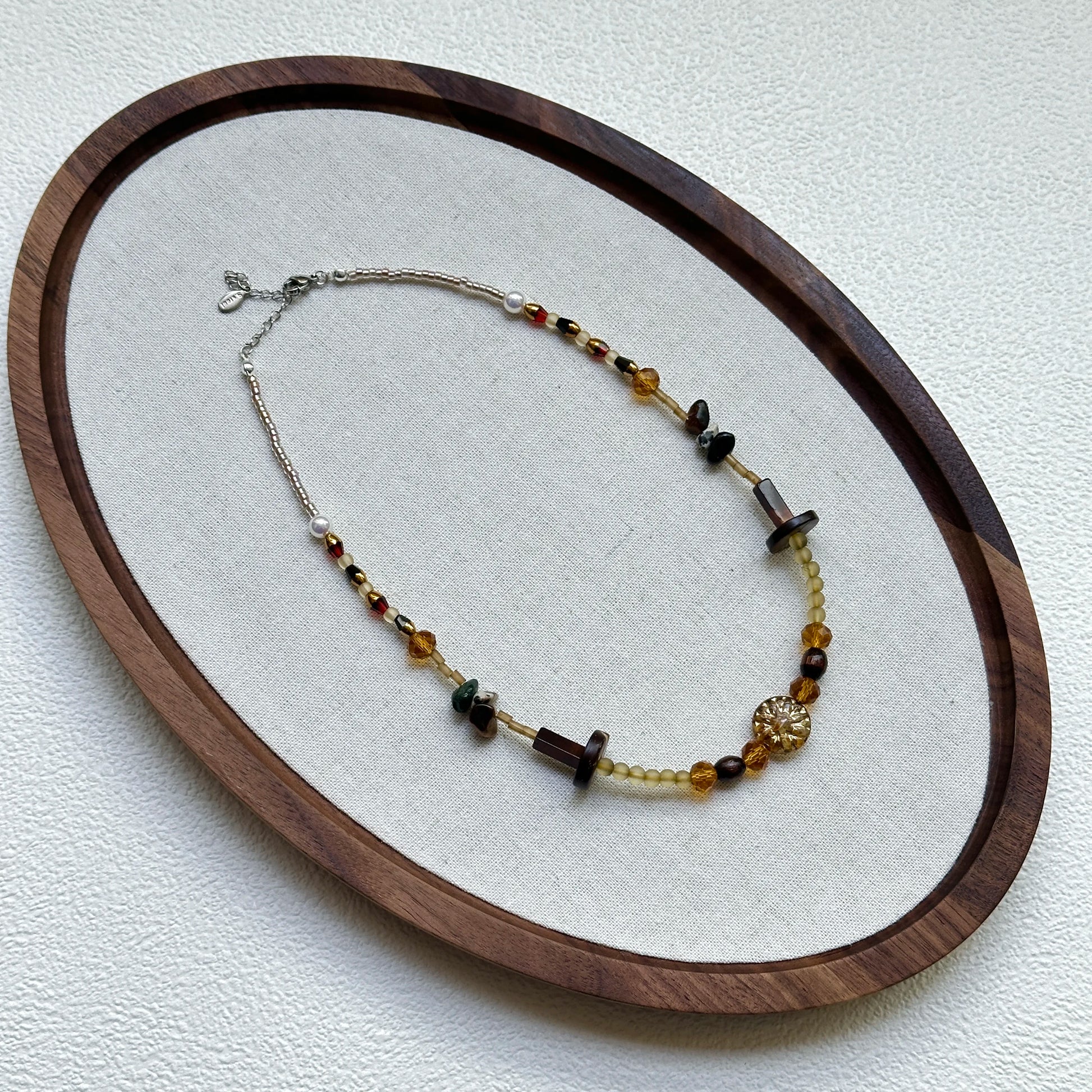 Marigold Ember Necklace displayed on an oval tray – warm amber, brown, and green beads with sunburst centerpiece