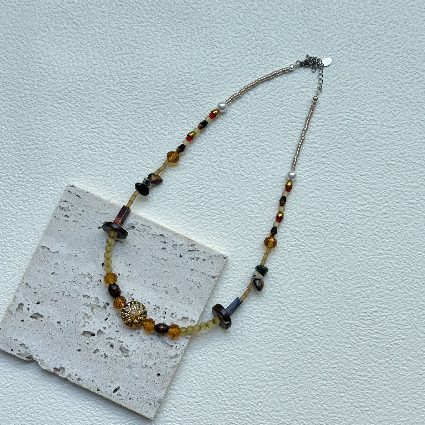 Flat lay of Marigold Ember Necklace on textured card, handcrafted amber–marigold palette with golden sunburst charm – Glazenya