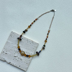 Flat lay of Marigold Ember Necklace on textured card, handcrafted amber–marigold palette with golden sunburst charm – Glazenya