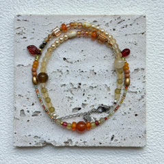 Flat lay of Golden Nectar Necklace on textured card – warm amber and gold palette with petite leaf accent