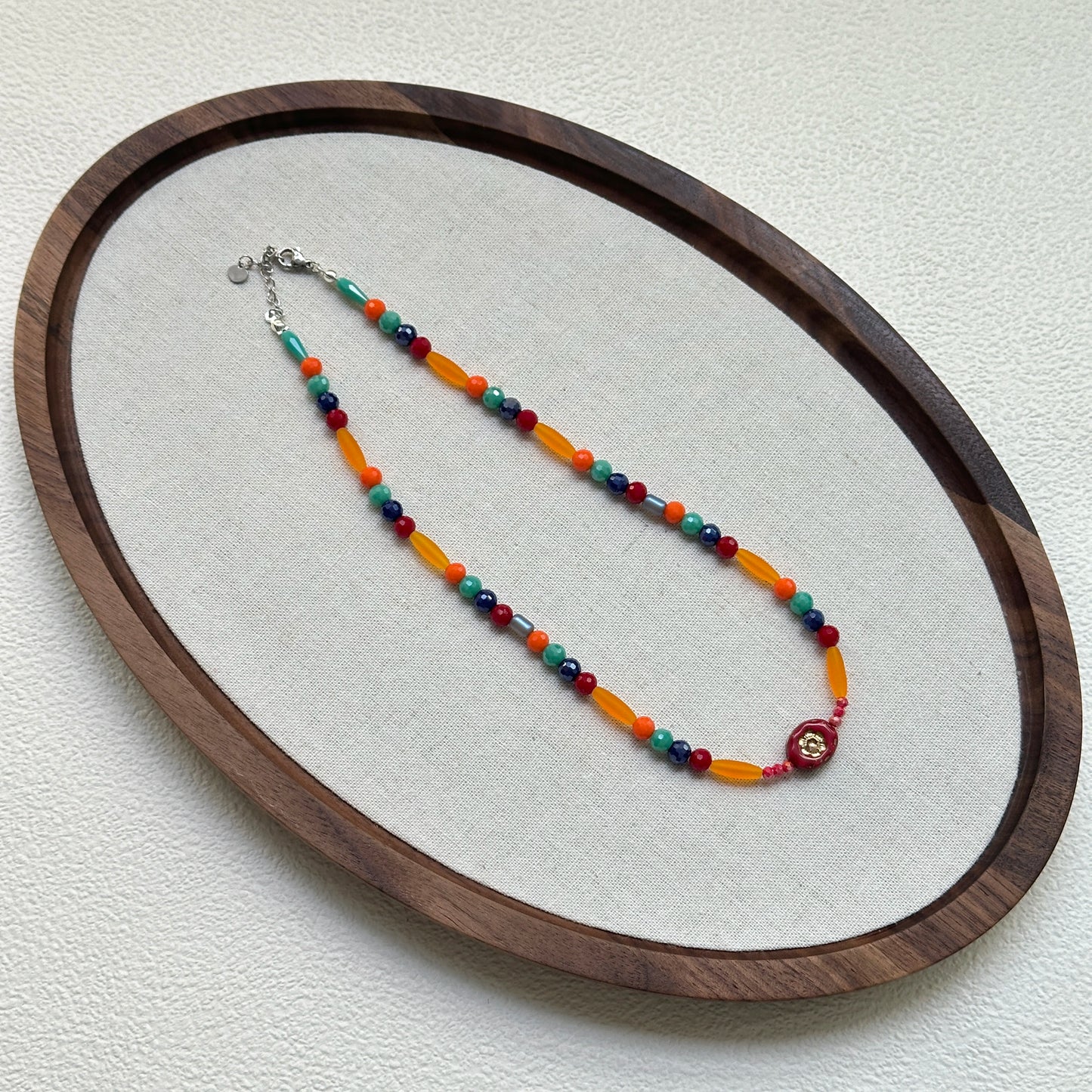 Sunburst Fiesta Necklace laid flat in circular wooden tray, showcasing playful red, orange, and turquoise beads
