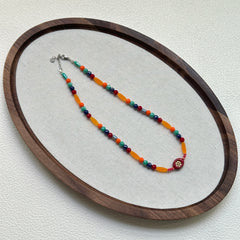 Sunburst Fiesta Necklace laid flat in circular wooden tray, showcasing playful red, orange, and turquoise beads