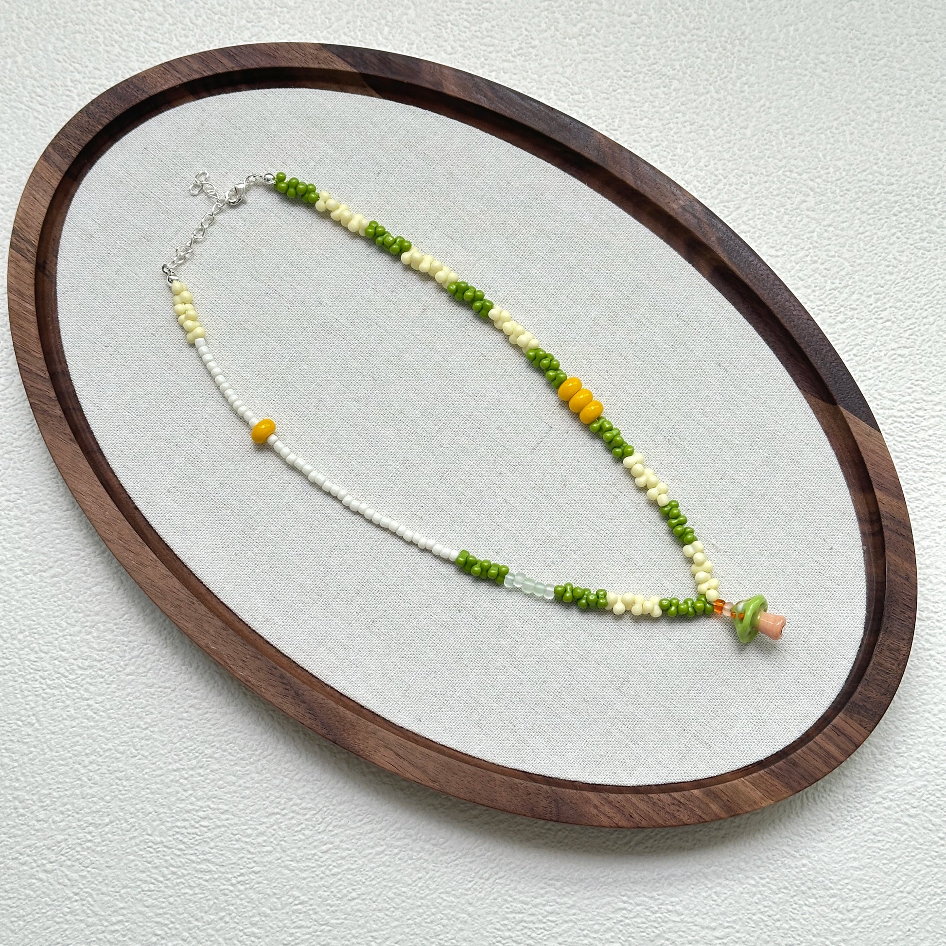 Forest Mushroom Necklace oval flat lay – handcrafted necklace featuring whimsical green mushroom pendant with fresh green and ivory beads by Glazenya
