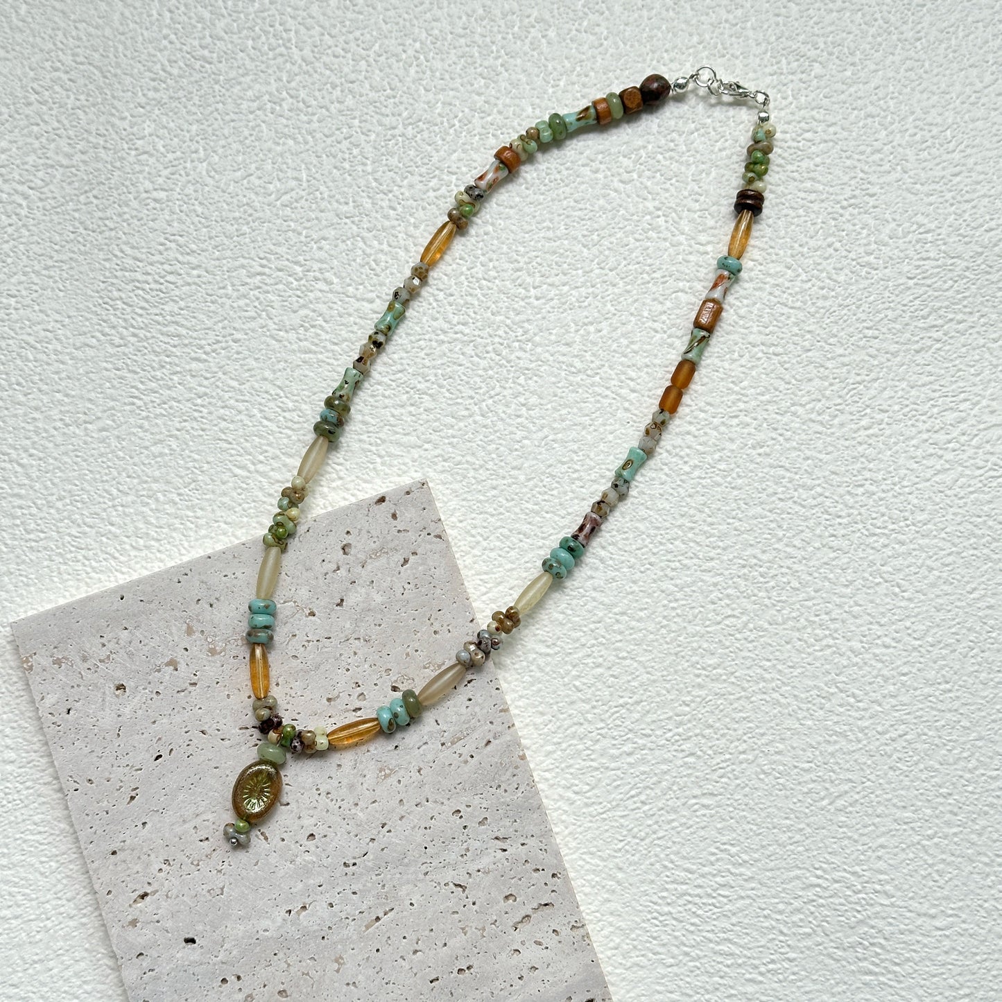 Verdant Amulet Necklace styled on white background – handmade necklace with earthy glass beads and amulet-inspired charm pendant by Glazenya