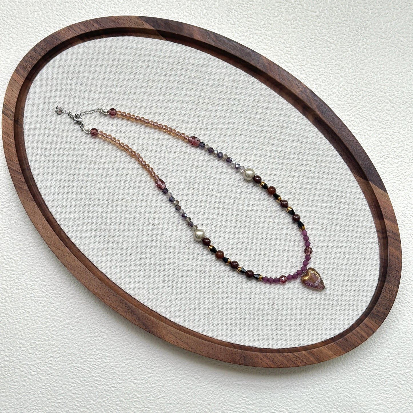 Amour Heart Necklace oval flat lay – handcrafted necklace featuring blush pink heart pendant with plum, crimson, and gold glass beads by Glazenya