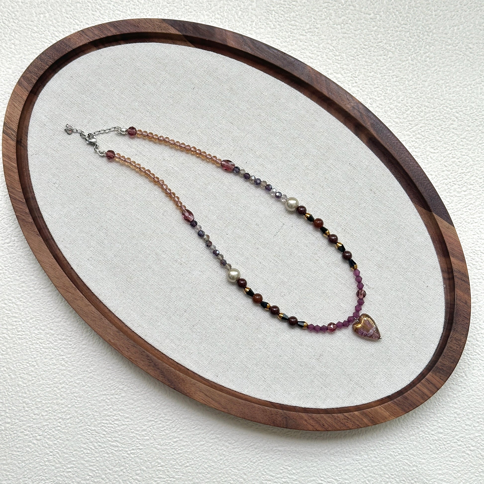Amour Heart Necklace oval flat lay – handcrafted necklace featuring blush pink heart pendant with plum, crimson, and gold glass beads by Glazenya