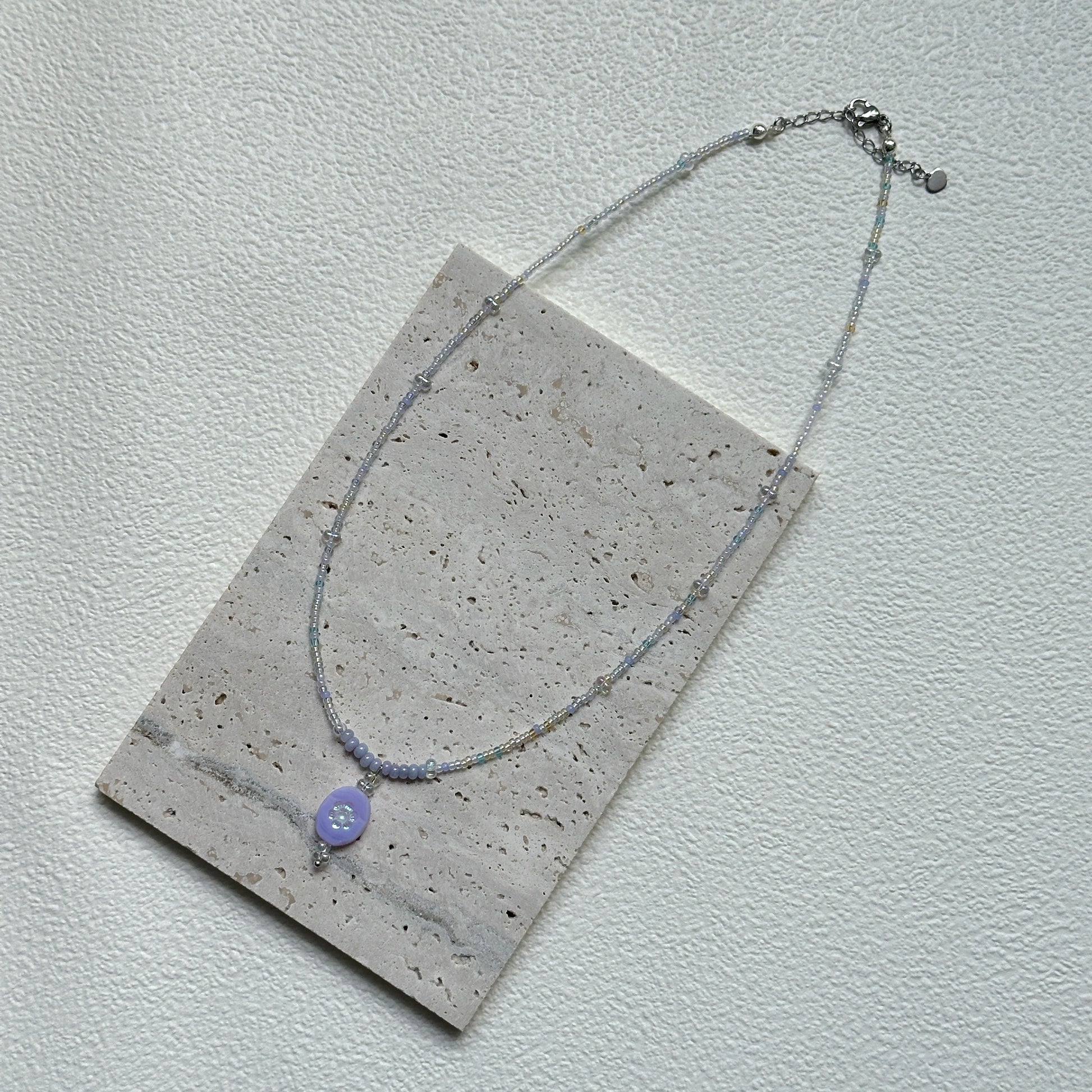 Handmade Aurora Dew Necklace laid flat, showing iridescent beads and delicate pendant details
