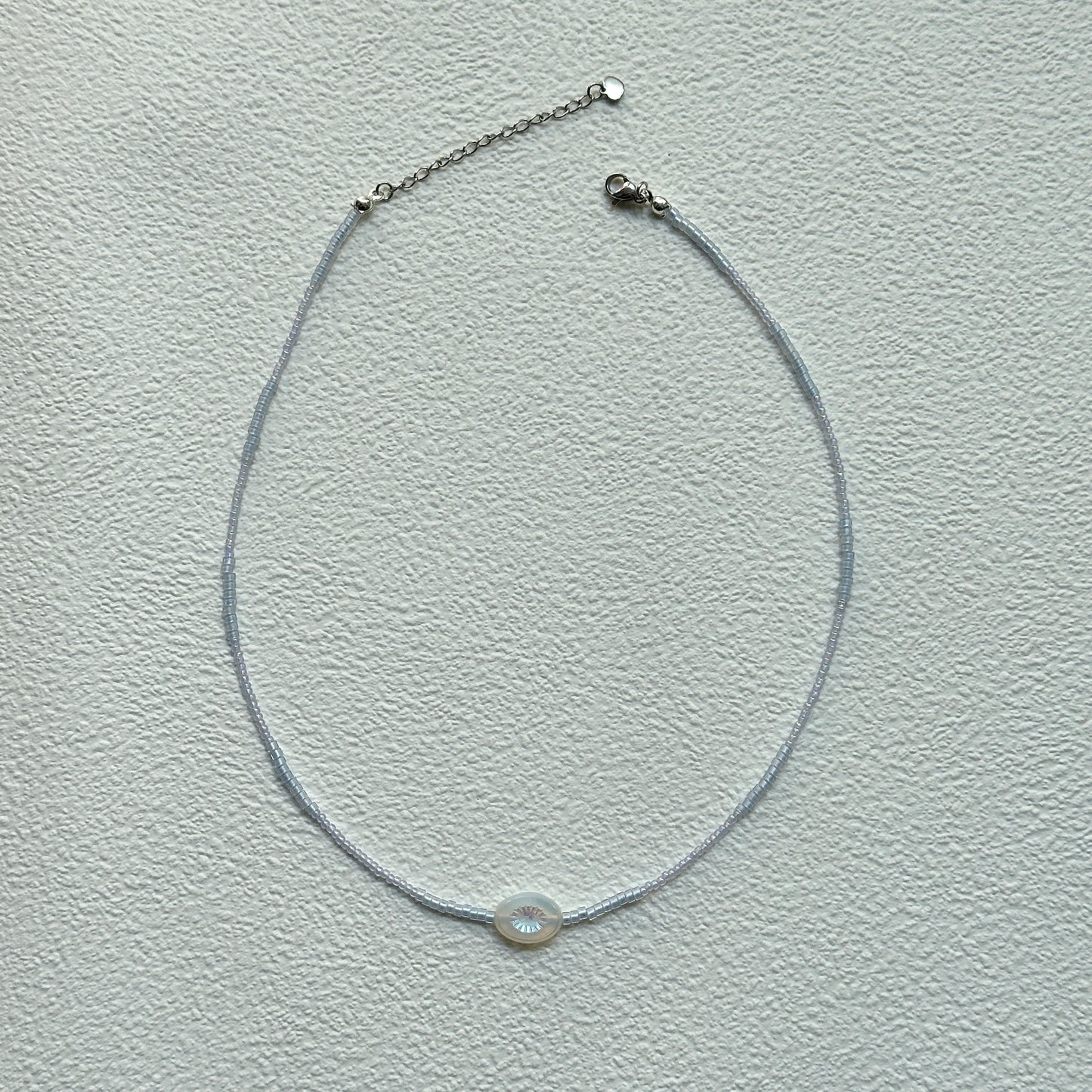 Minimalist Dawn Halo Necklace laid flat with delicate seed beads and circular engraved charm