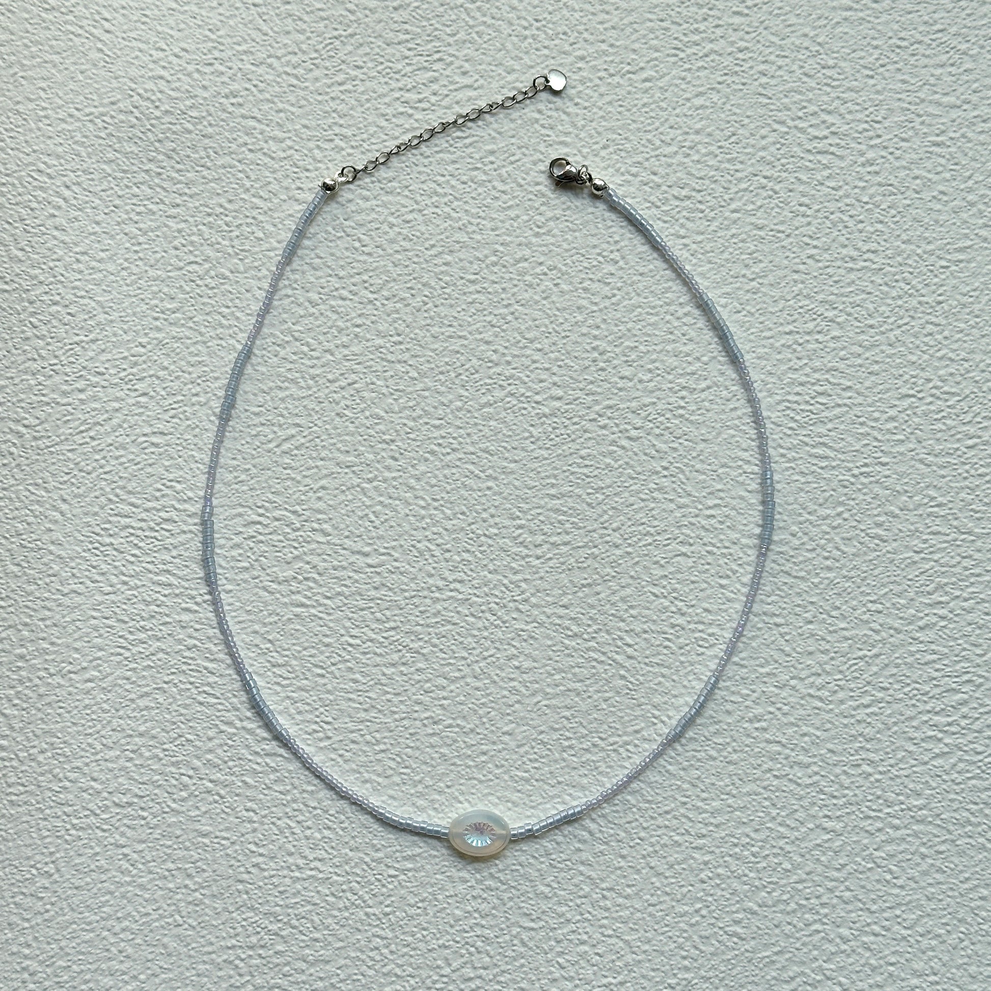 Minimalist Dawn Halo Necklace laid flat with delicate seed beads and circular engraved charm