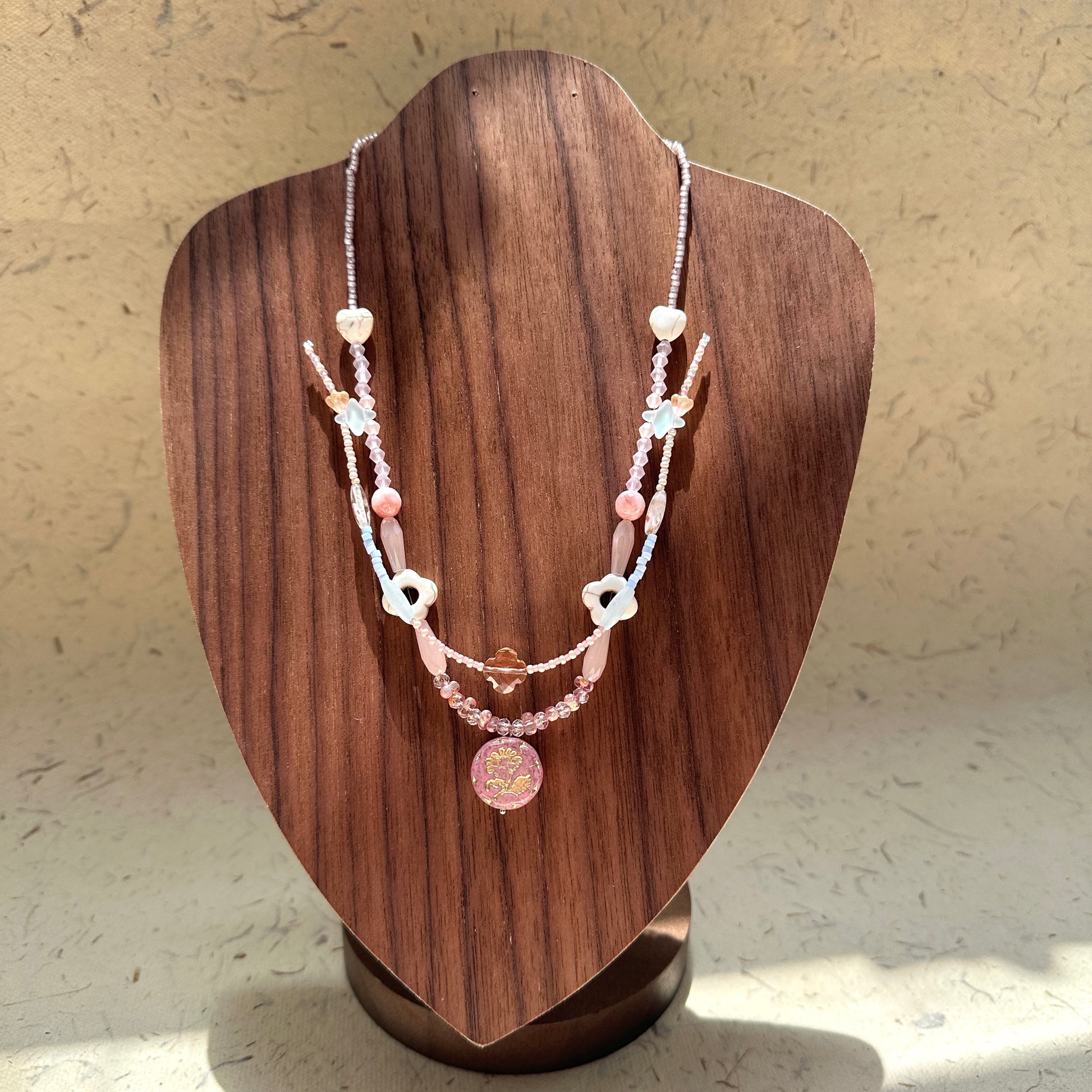 Sakura Medallion Necklace on wood display bust — double-strand pastel beads with heart accents and a sakura medallion charm