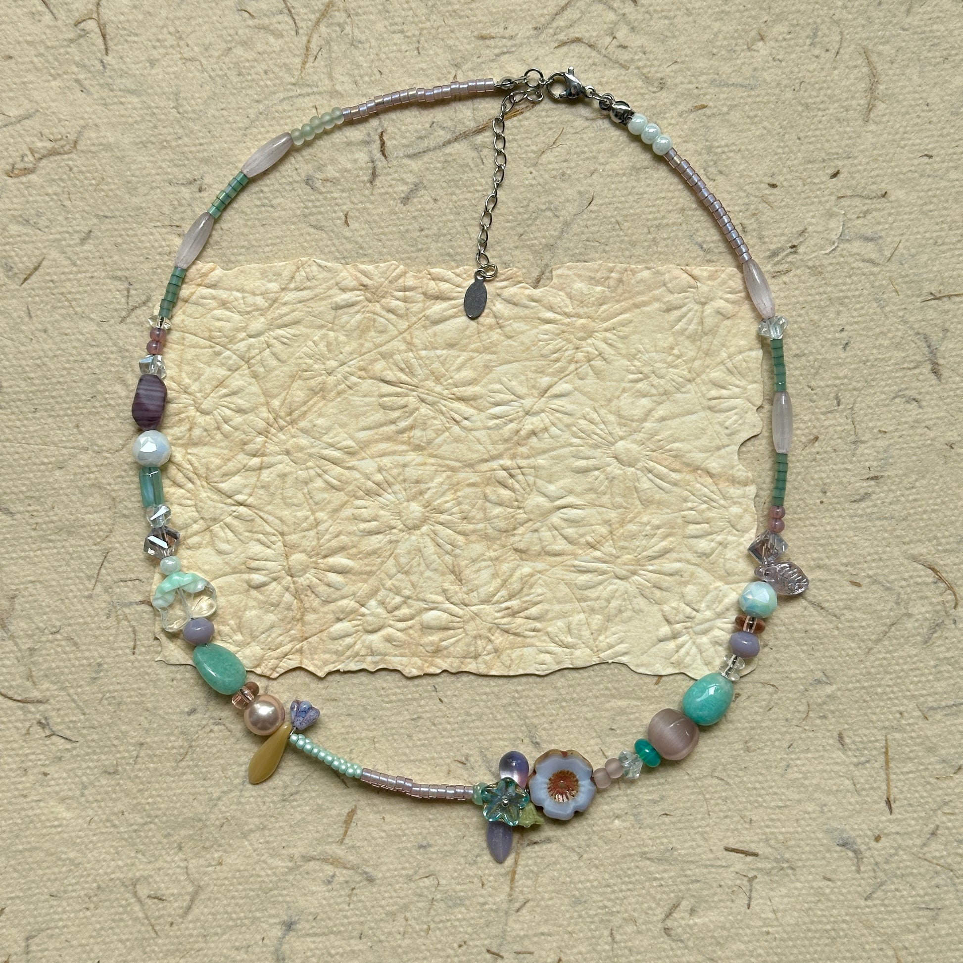 Seafoam Petal Necklace — top-down view showing full necklace on textured paper; seafoam and lilac pastel beads with floral/petal accents
