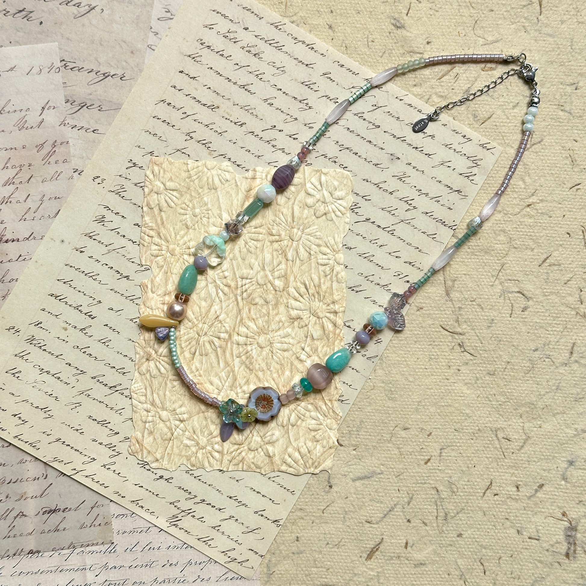 Seafoam Petal Necklace — angled view on textured paper highlighting the bead mix and petal-shaped accent detail