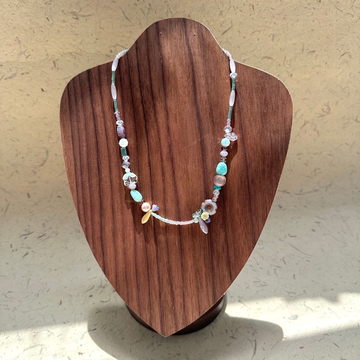 Seafoam Petal Necklace on wood display bust — pastel beads in seafoam, lilac and pearl-white with floral and petal-shaped accents