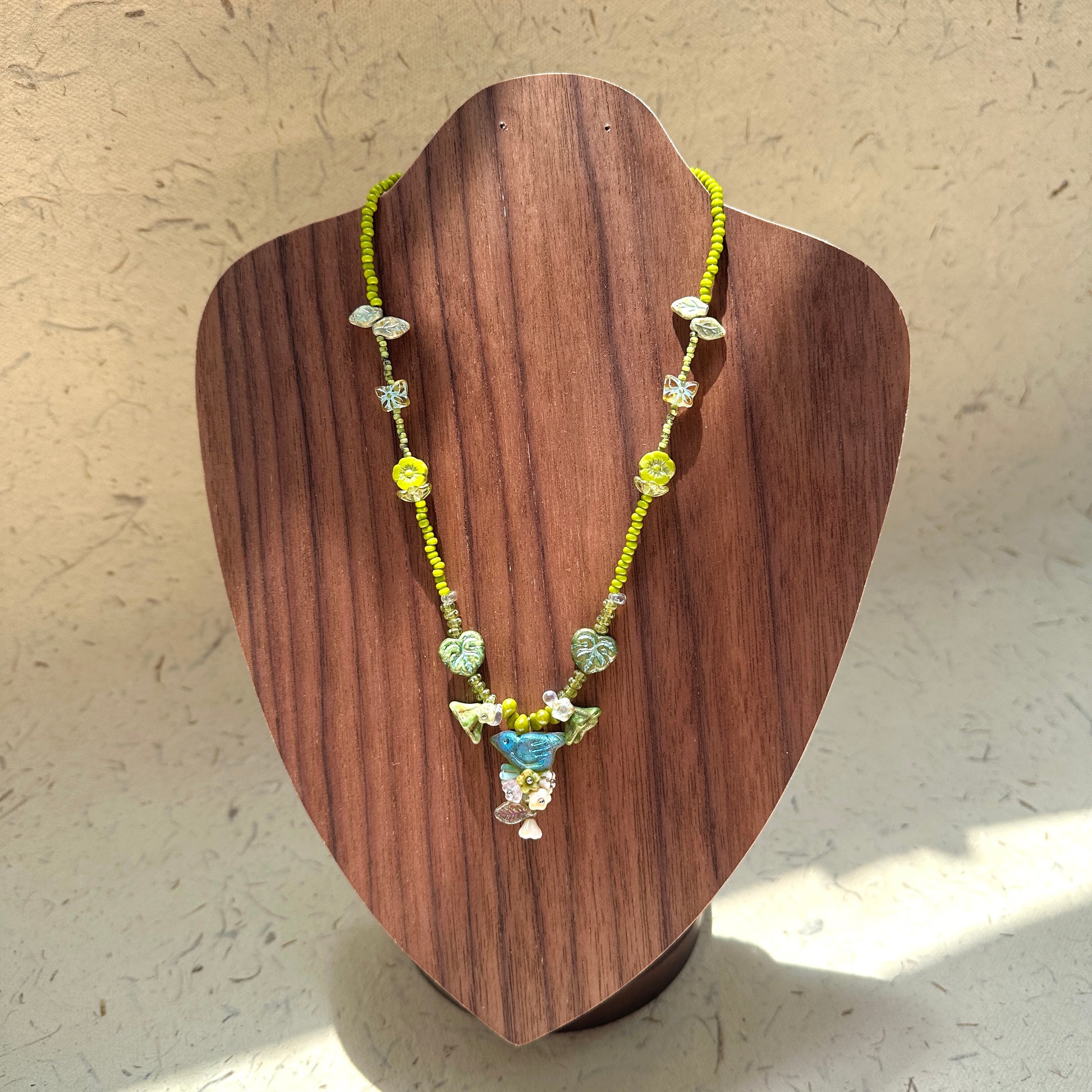 Limeleaf Bouquet Necklace on wood display bust — lime-green seed beads with leaf and butterfly accents, bouquet-style charm