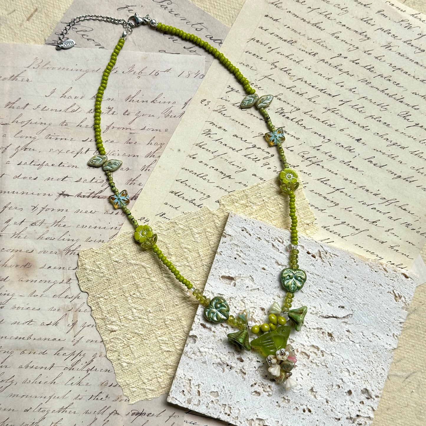 Limeleaf Bouquet Necklace — flat lay on vintage papers; lime-green seed beads with leaf and butterfly accents and a bouquet-style focal charm