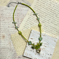 Limeleaf Bouquet Necklace — flat lay on vintage papers; lime-green seed beads with leaf and butterfly accents and a bouquet-style focal charm