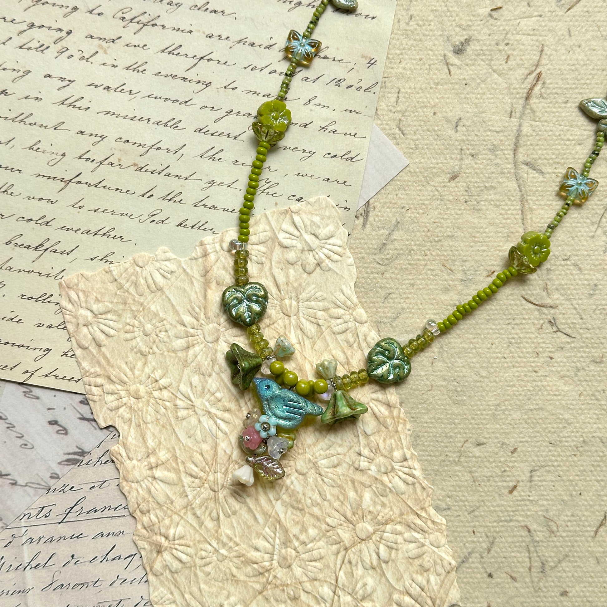 Limeleaf Bouquet Necklace — top-down view on textured paper; full necklace in lime and soft-green tones with leaf/butterfly details