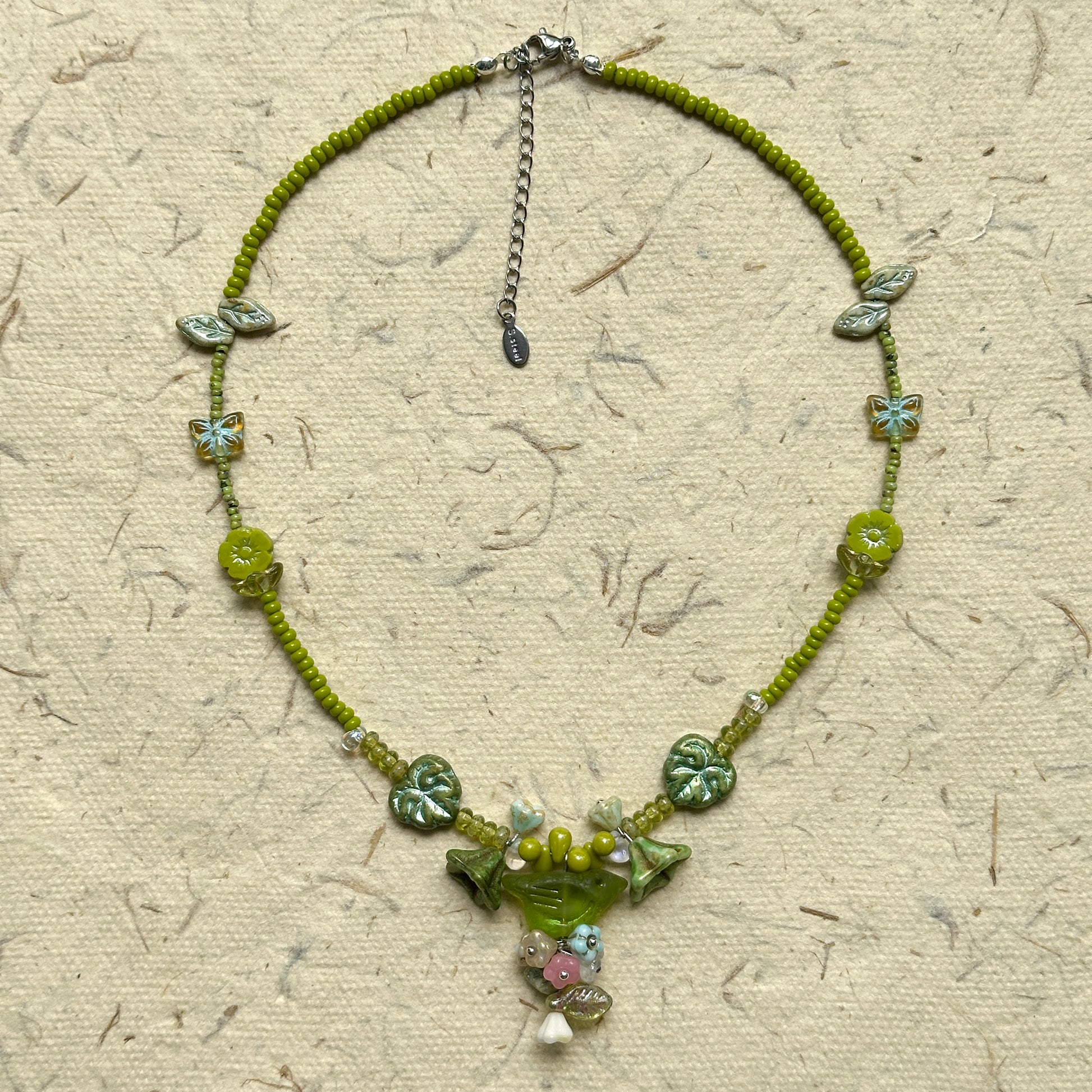 Limeleaf Bouquet Necklace — circle layout on neutral textured paper showing bead palette and bouquet-style charm