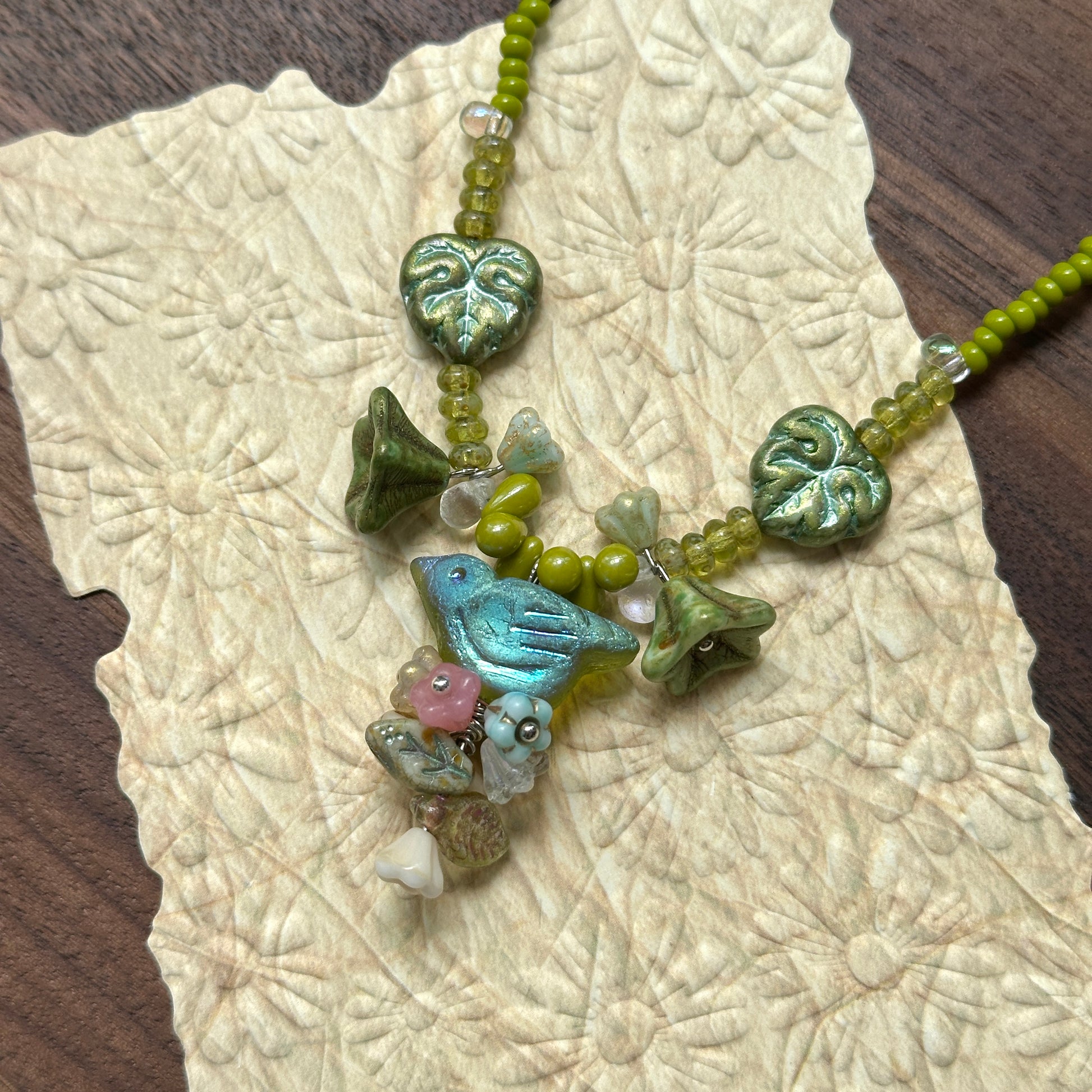 Limeleaf Bouquet Necklace — angled close-up on textured paper highlighting the bouquet-style focal, lime beads, and leaf accents