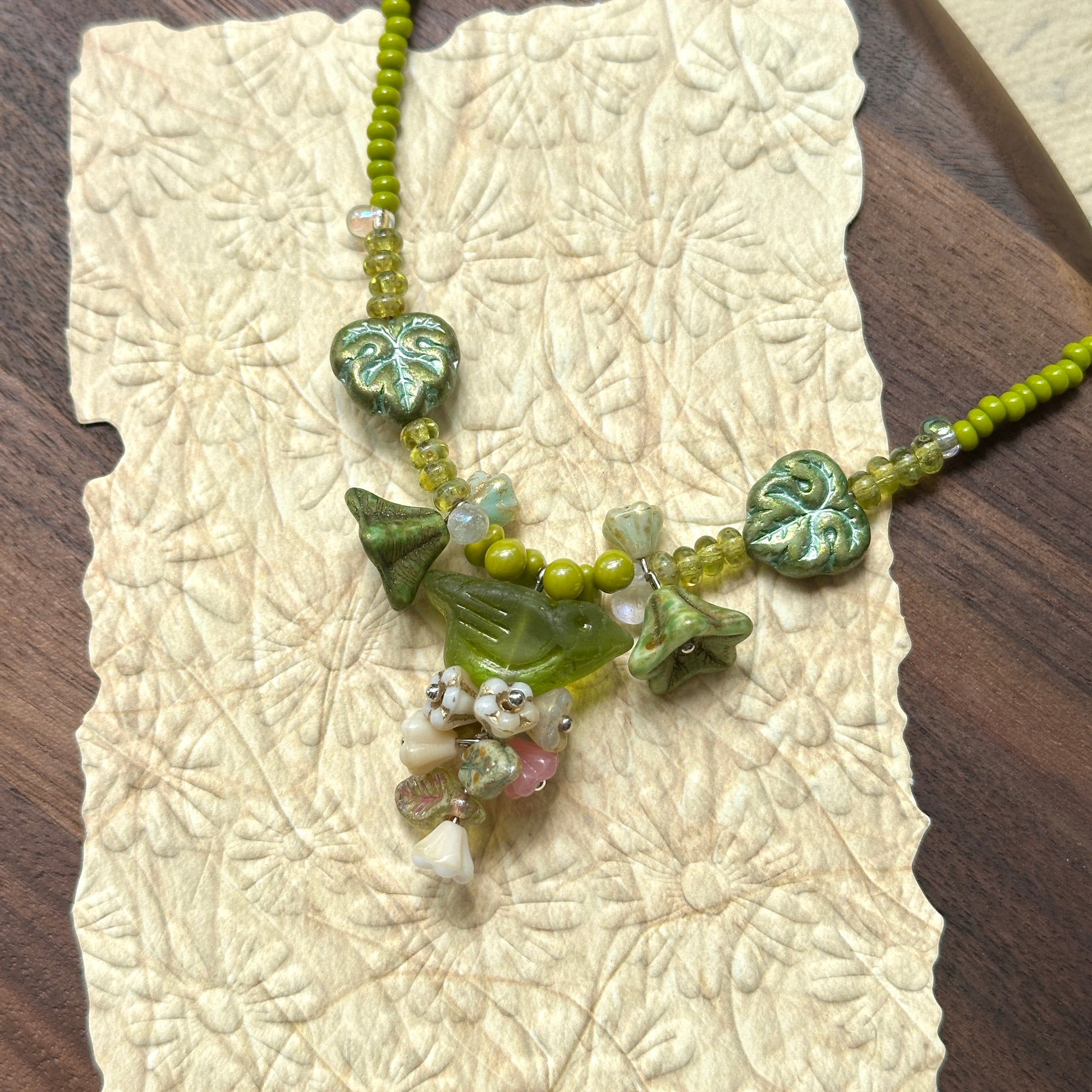 Limeleaf Bouquet Necklace — angled close-up on textured paper highlighting the bouquet-style focal, lime beads, and leaf accents1