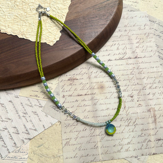 Citrus Wave Necklace — flat lay on textured papers; lime and aqua beads with striped segments and a wave medallion