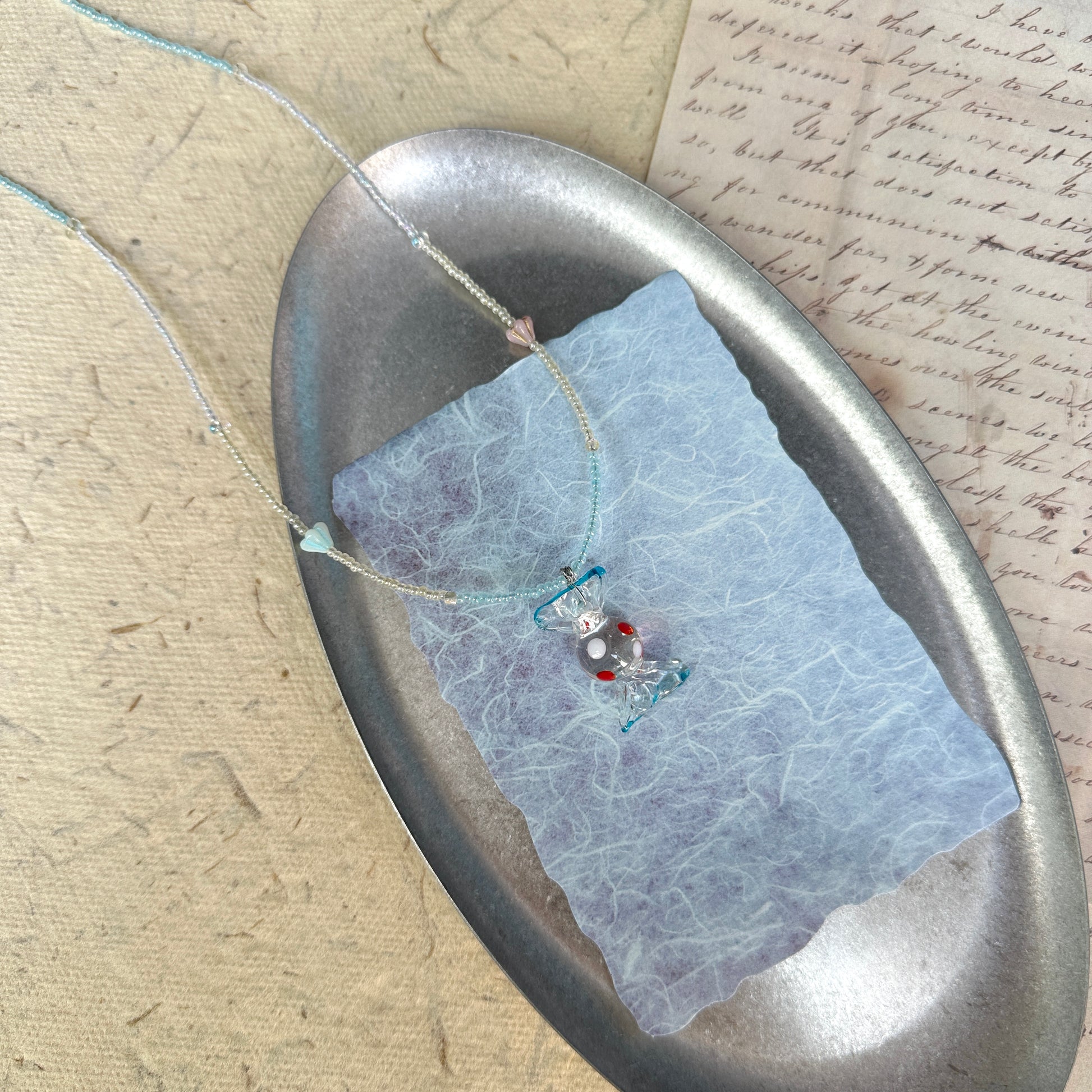 Ocean Bonbon Necklace — circle layout on textured paper showing pastel aqua/pearl palette and candy pendant