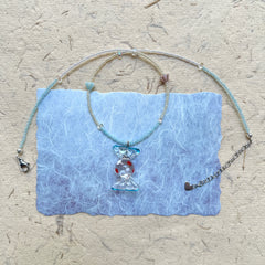 Ocean Bonbon Necklace — flat lay on textured paper; aqua and pearl beads with a glass candy pendant featuring red polka dots