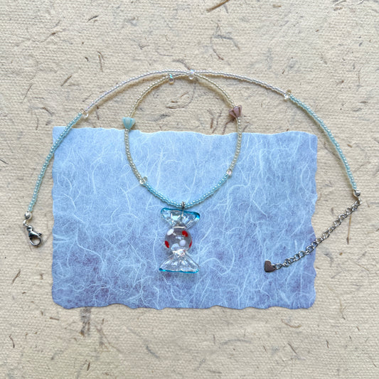 Ocean Bonbon Necklace — flat lay on textured paper; aqua and pearl beads with a glass candy pendant featuring red polka dots