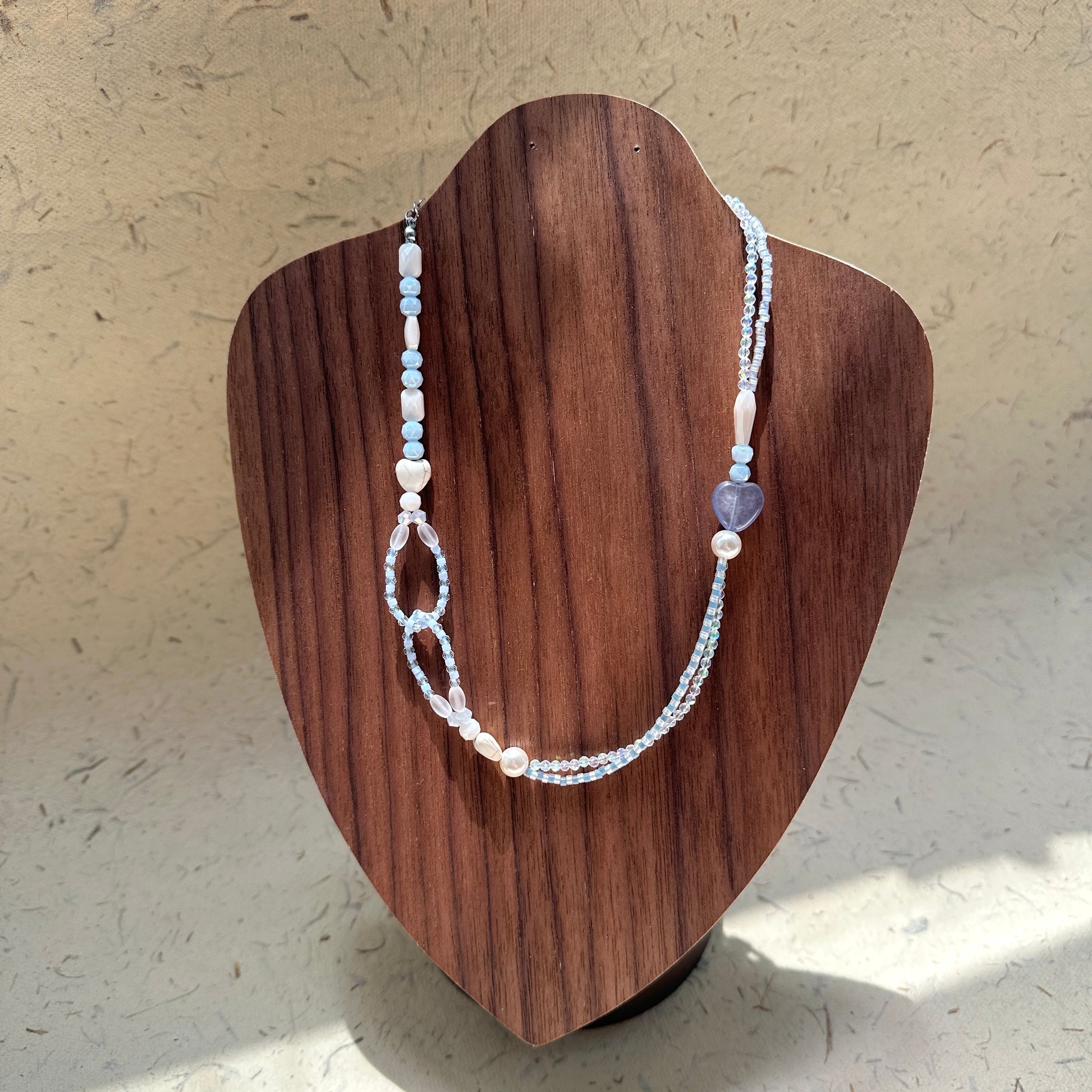 Lunar Mist Necklace on wood display bust — double-strand icy-blue and pearl-white beads with a heart accent and loop detail