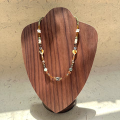 Sage & Saffron Necklace on wood display bust — sage-green and amber beads with speckled heart accents and a dotted cube focal