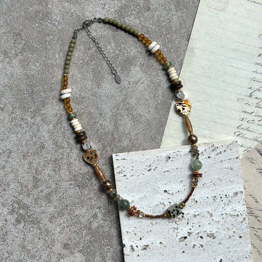 Sage & Saffron Necklace — flat lay on textured paper; sage-green and honey-amber beads with speckled heart accents and a dotted cube focal