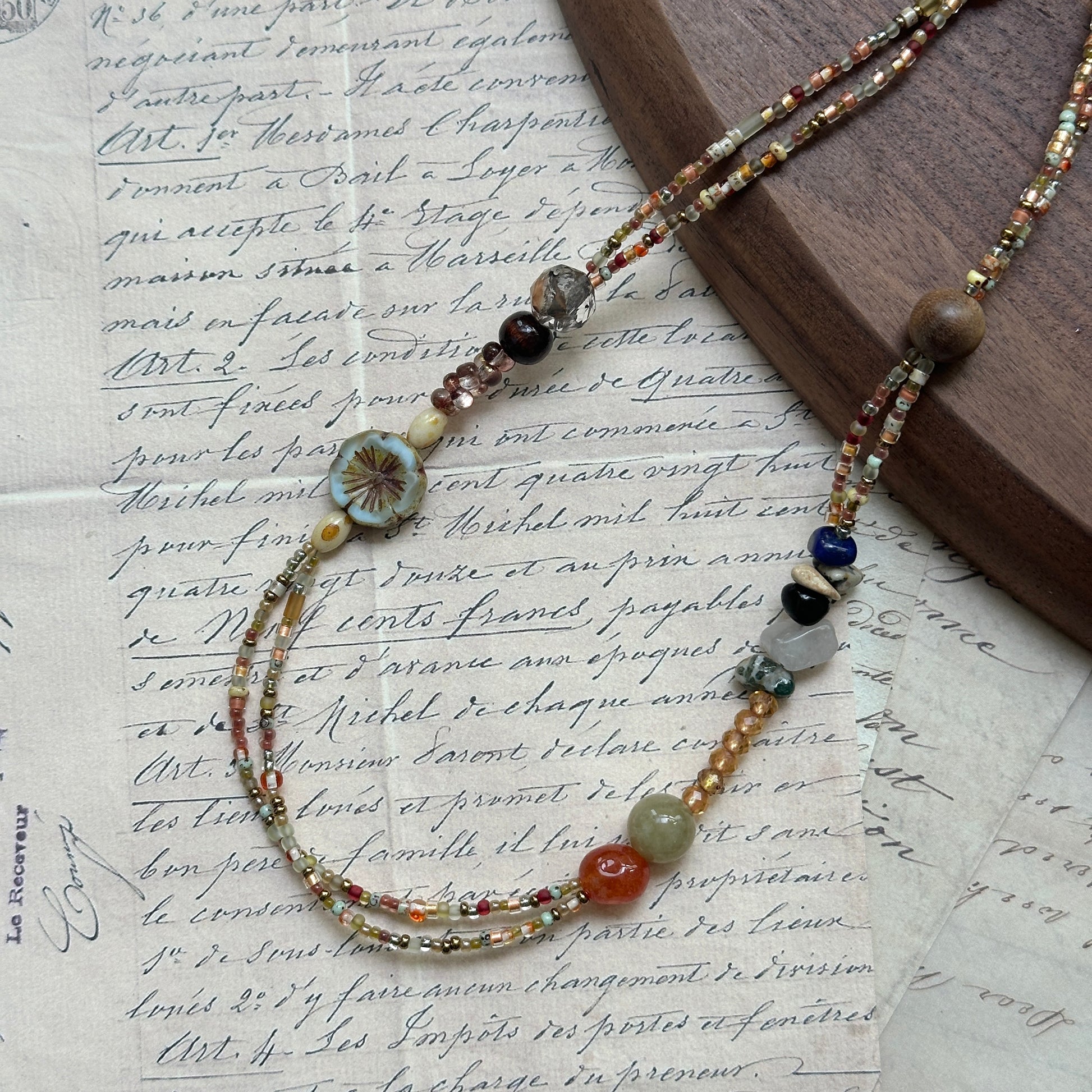 Marigold Mosaic Necklace — flat lay on textured papers; warm amber/marigold palette with floral coin and mixed beads