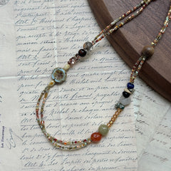 Marigold Mosaic Necklace — flat lay on textured papers; warm amber/marigold palette with floral coin and mixed beads